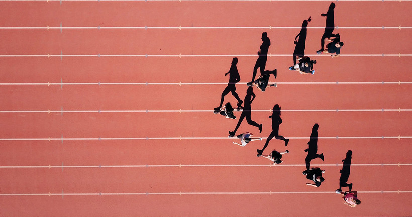 Mehrere Läufer auf einem Marathonfeld - Agilität als Schlüsselfaktor der Digitalisierung Auf dem Bild sieht man mehrere Marathon-Läufer auf einem roten Sportfeld von oben fotografiert.