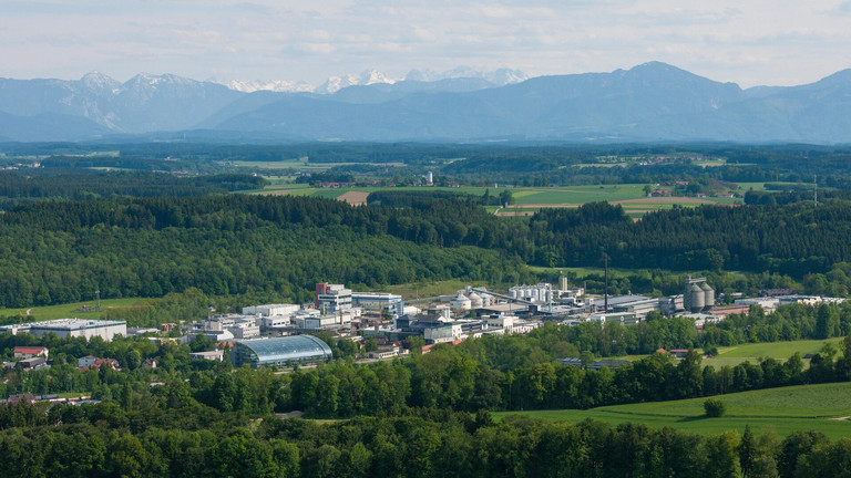 Luftaufnahme des Alzchem-Werks inmitten grüner Landschaft mit Blick auf die Alpen im Hintergrund